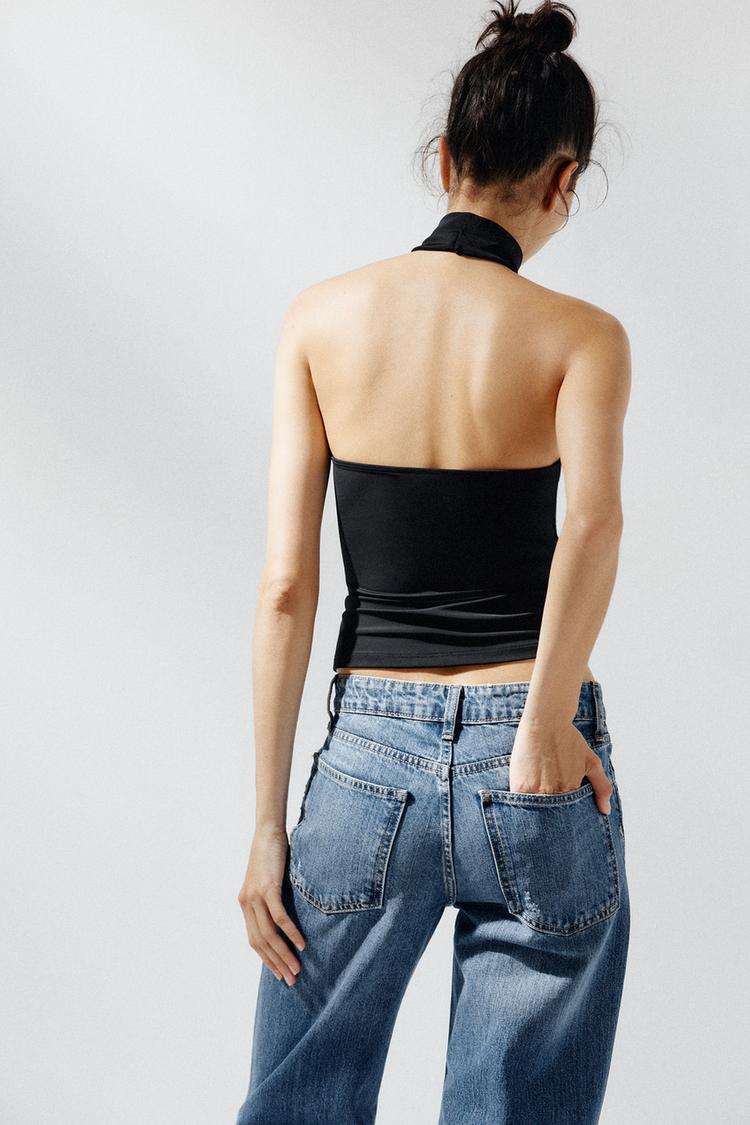 Σετ με μαύρο τοπ χωρίς πλάτη και μπλε τζιν με ορατές πίσω τσέπες.