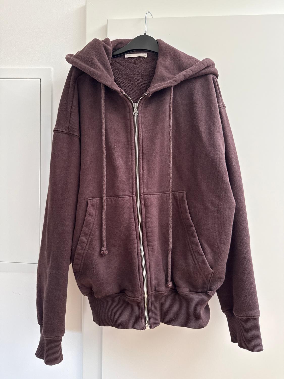 Brown hoodie hanging on a black hanger, with a front zip and adjustable drawstrings, on a white background.