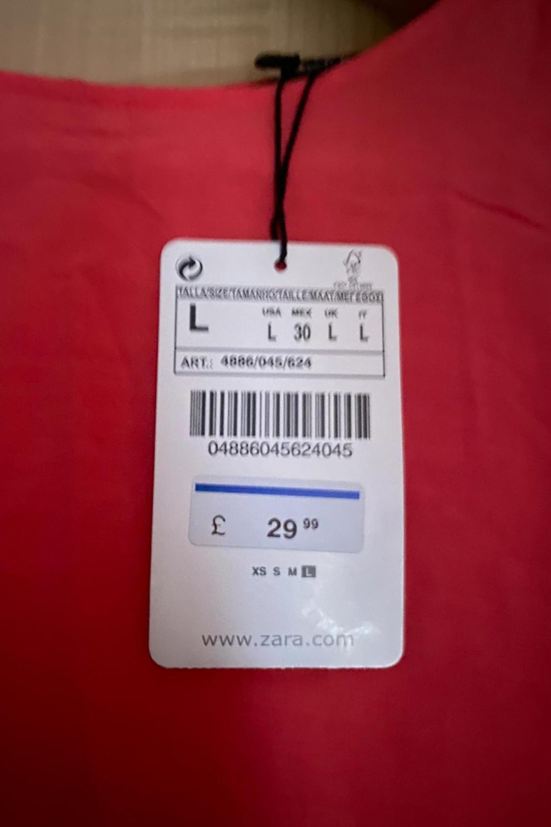 Detail of price and size label on red garment. Text: 'www.zara.com', '£29.99', 'L', 'ART: 4886/045/624'.