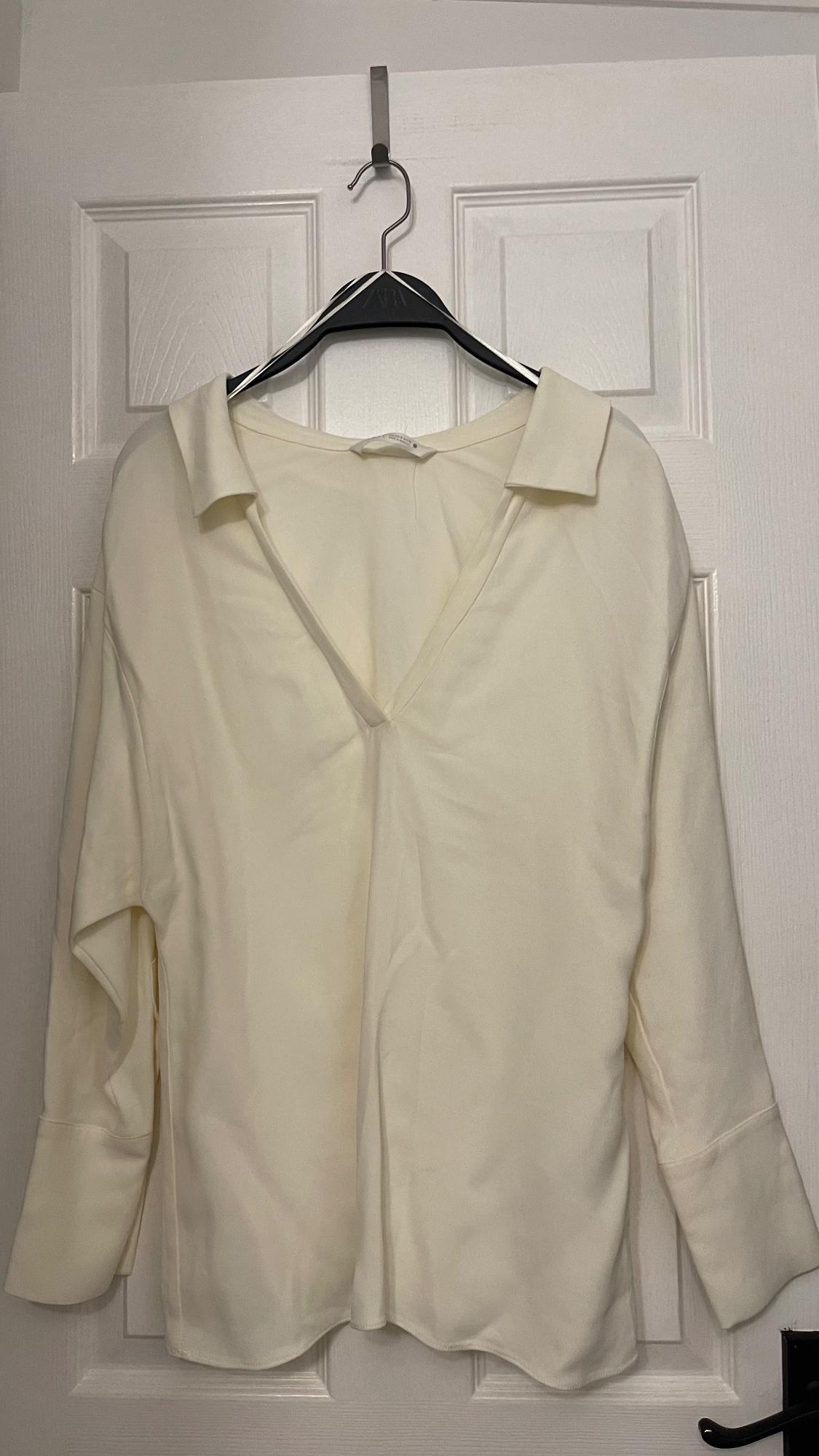 White long-sleeved V-neck shirt, hanging on a black hanger over a white door.