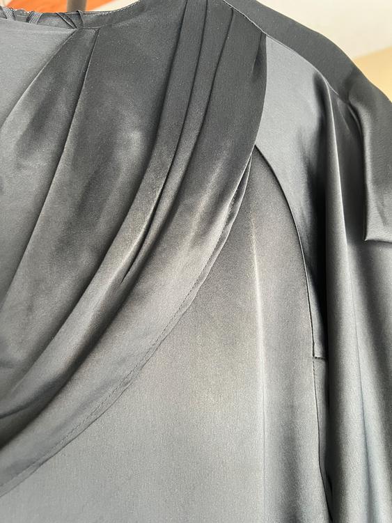 Detail of black fabric with soft folds and satin texture, captured up close. Partially visible background in light tones.
