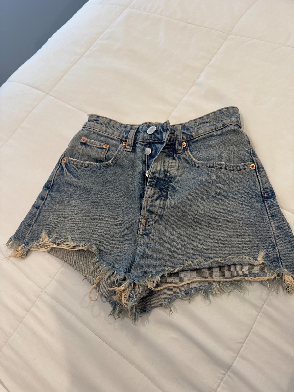 Distressed denim shorts with frayed hem, metal buttons and pockets, on a white quilt.