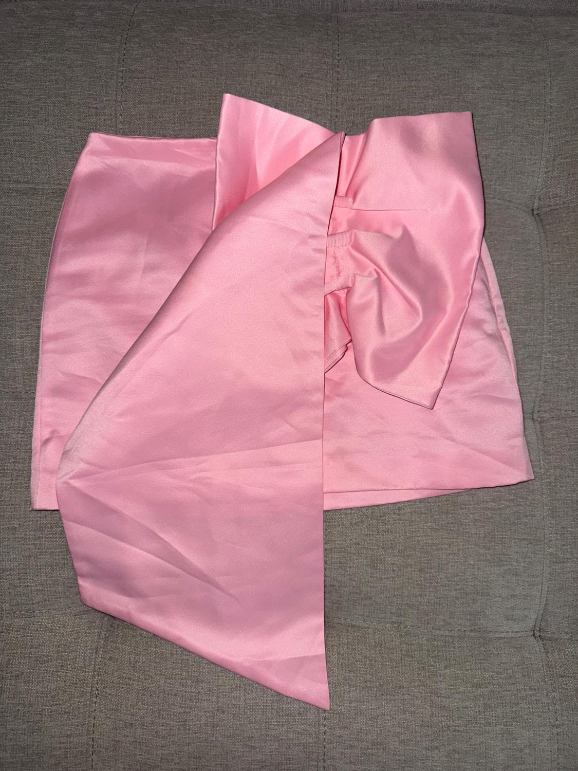 Satin pink skirt with large bow, placed on a textured gray background.