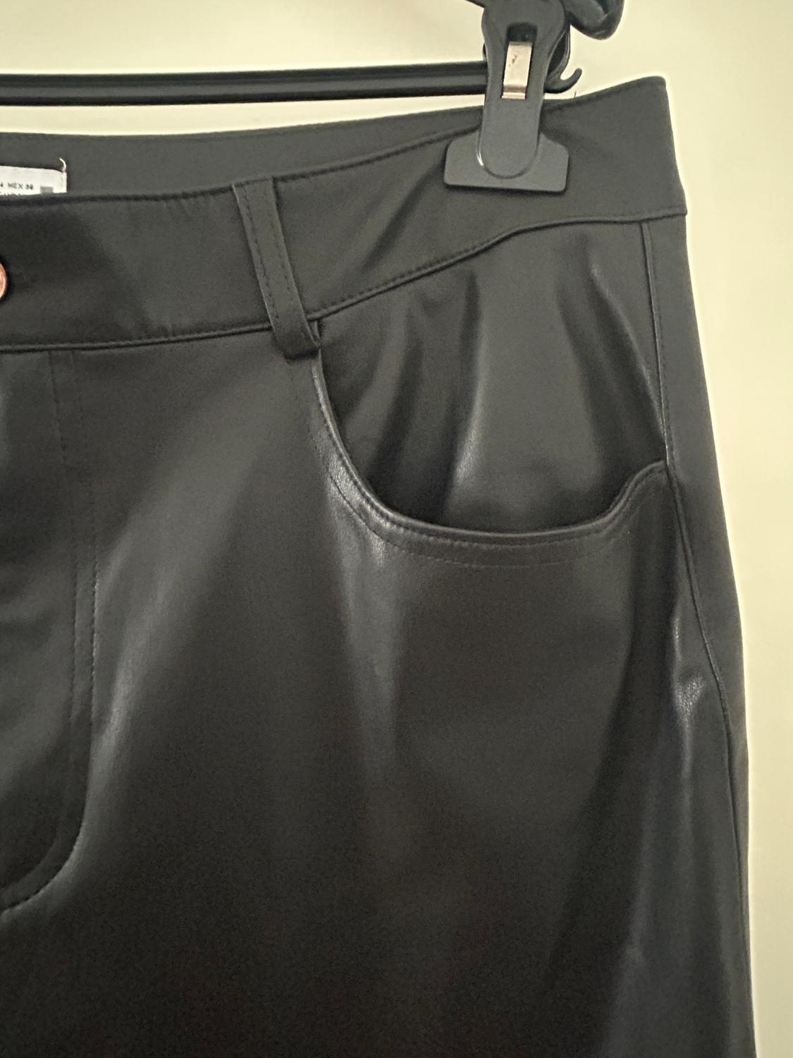 Black trousers hanging on a hanger, showing detail of the front pocket and waistband. Fabric with a glossy finish.