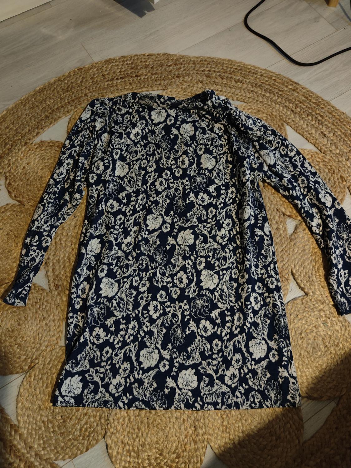 Long-sleeved dress with a white floral print on a dark blue background, placed on a jute rug on a light-coloured floor.