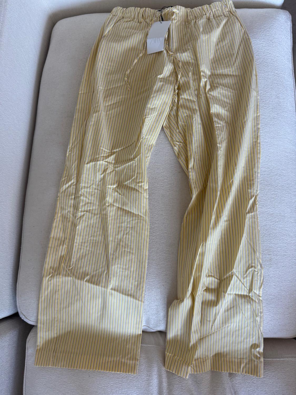 Yellow trousers with thin vertical stripes on a beige sofa, with a white tag hanging from the elasticated waist.