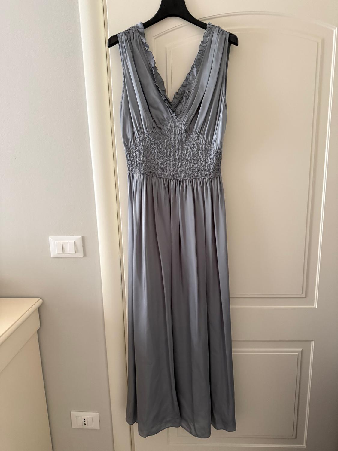 Long grey sleeveless dress with a V-neck and ruched detailing, hanging on a black hanger over a white door.