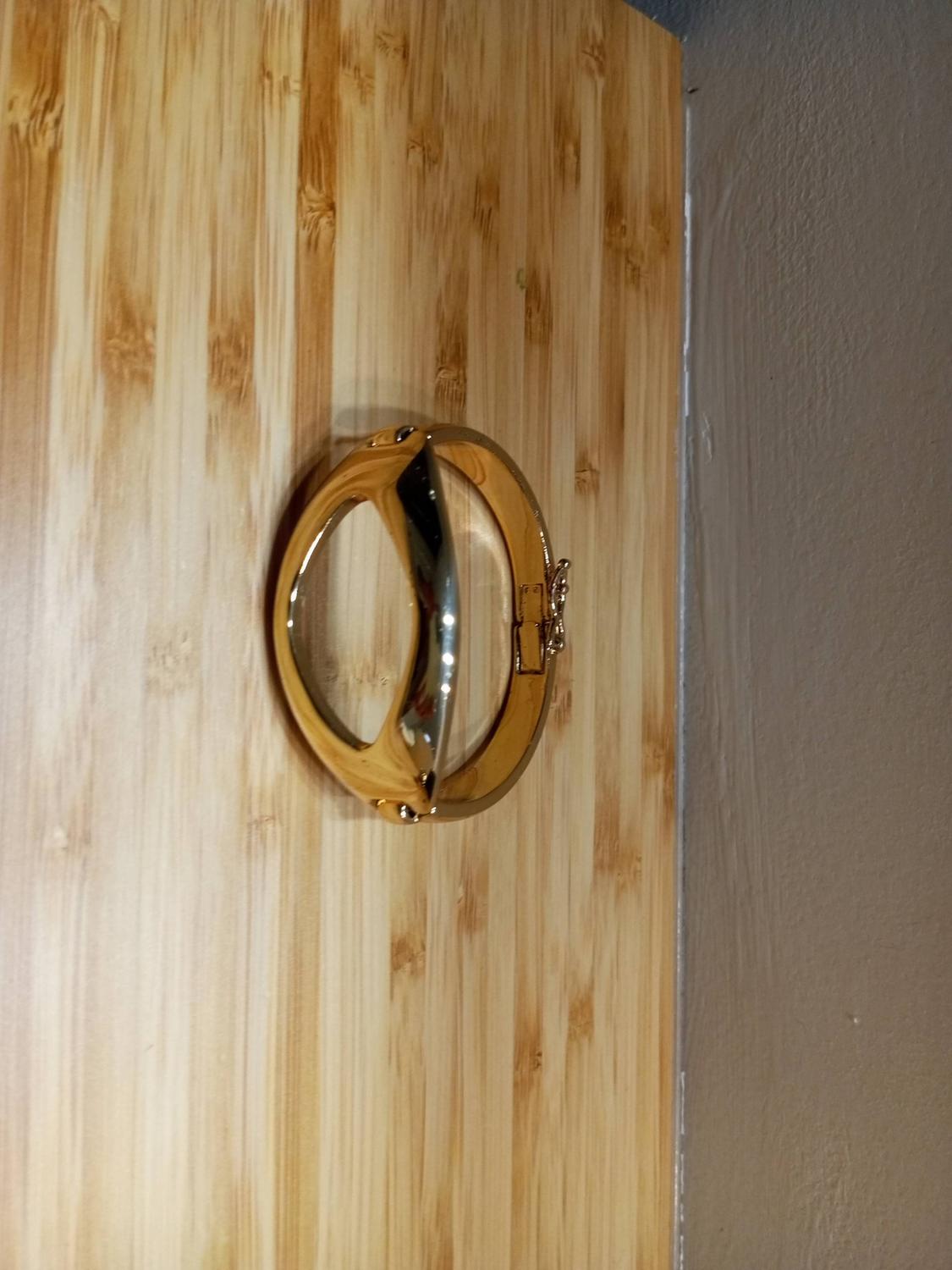Gold-coloured metal bracelet with a circular design, hanging on a light wooden wall.
