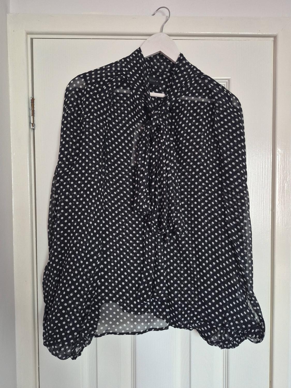 Semi-transparent black blouse with white polka dots and a necktie, hanging on a coat hanger over a white door.