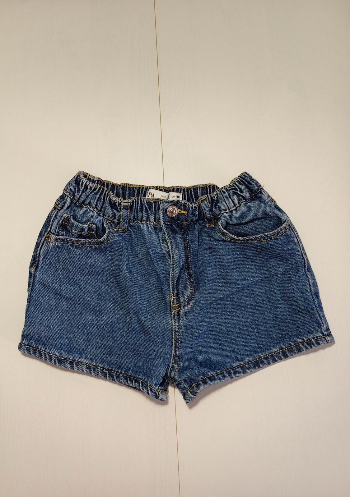 Blue denim shorts with an elasticated waist on a light surface. Relaxed fit. Label with text ZARA size CM 110.