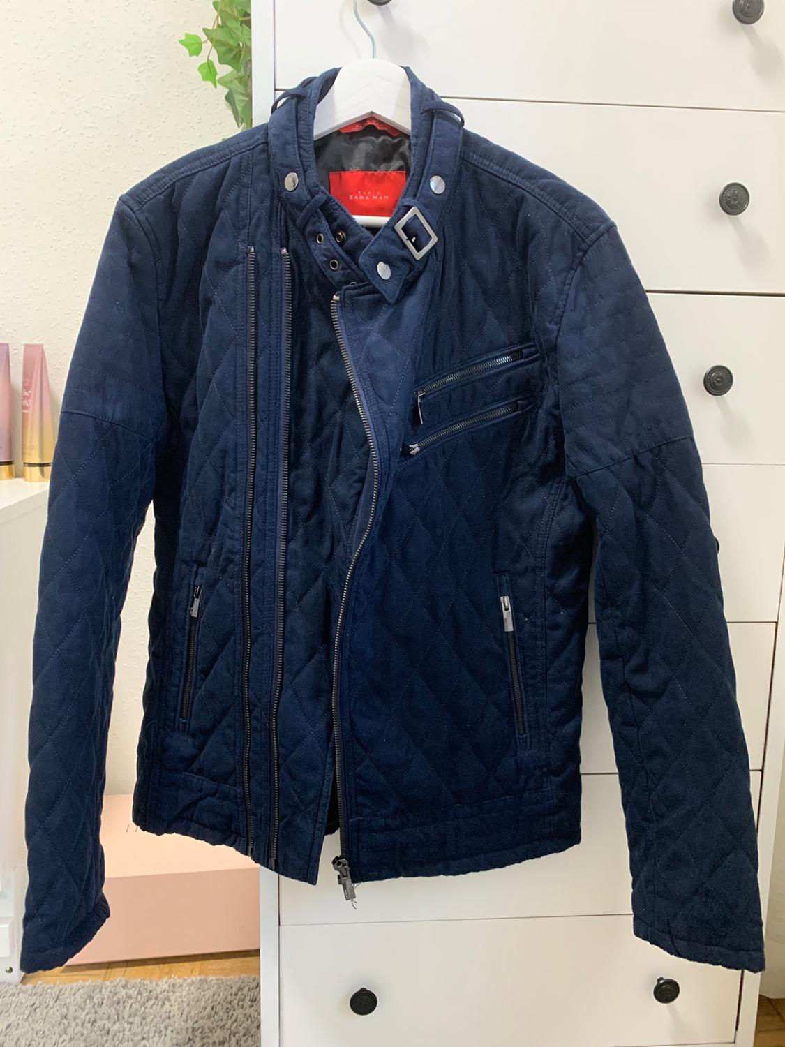 Front view of a blue padded jacket with zips and side pockets.