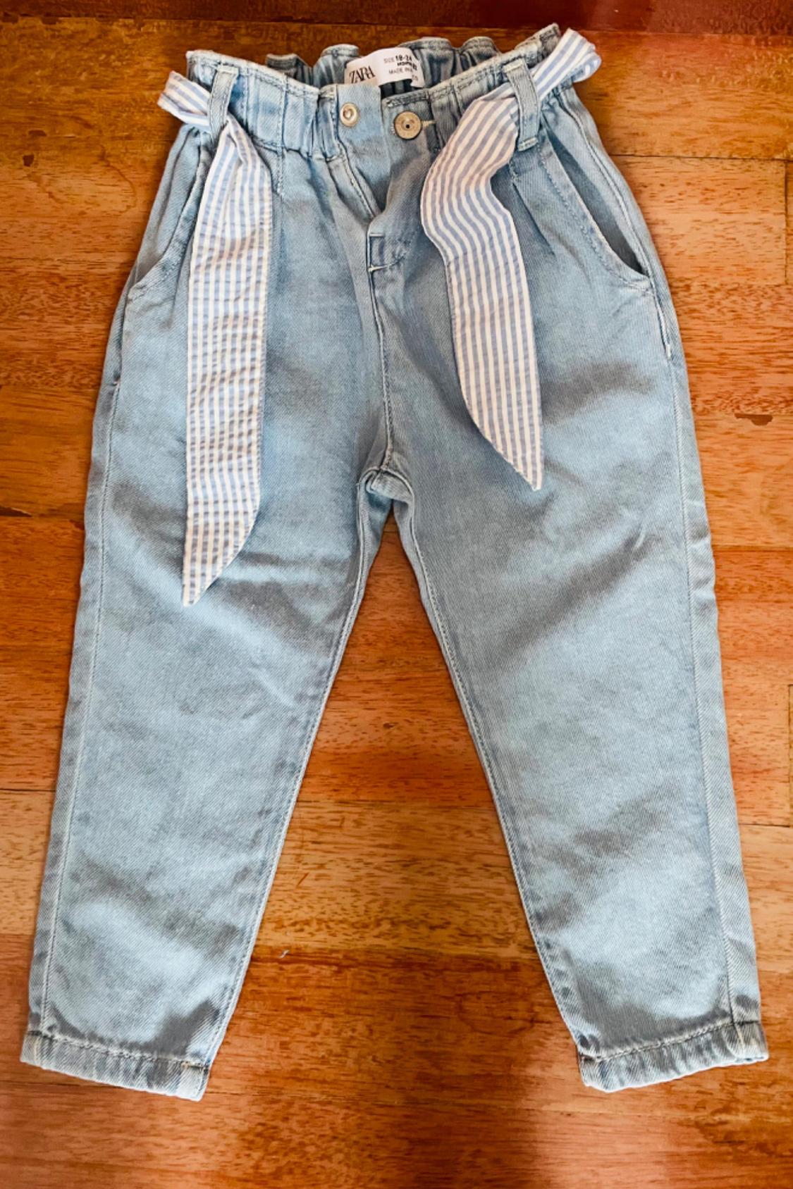Front view of light blue trousers with a striped belt and side pockets.