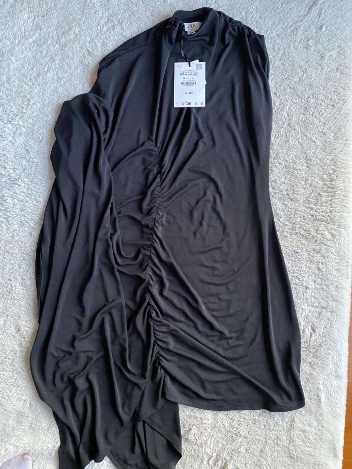 Black dress with central ruching, visible label with "XS" and "ZARA" text, on a light surface.