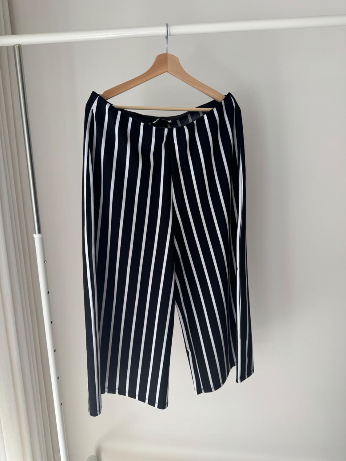 Wide-leg black and white vertical striped trousers hanging on a wooden hanger on a white metal clothes rail.