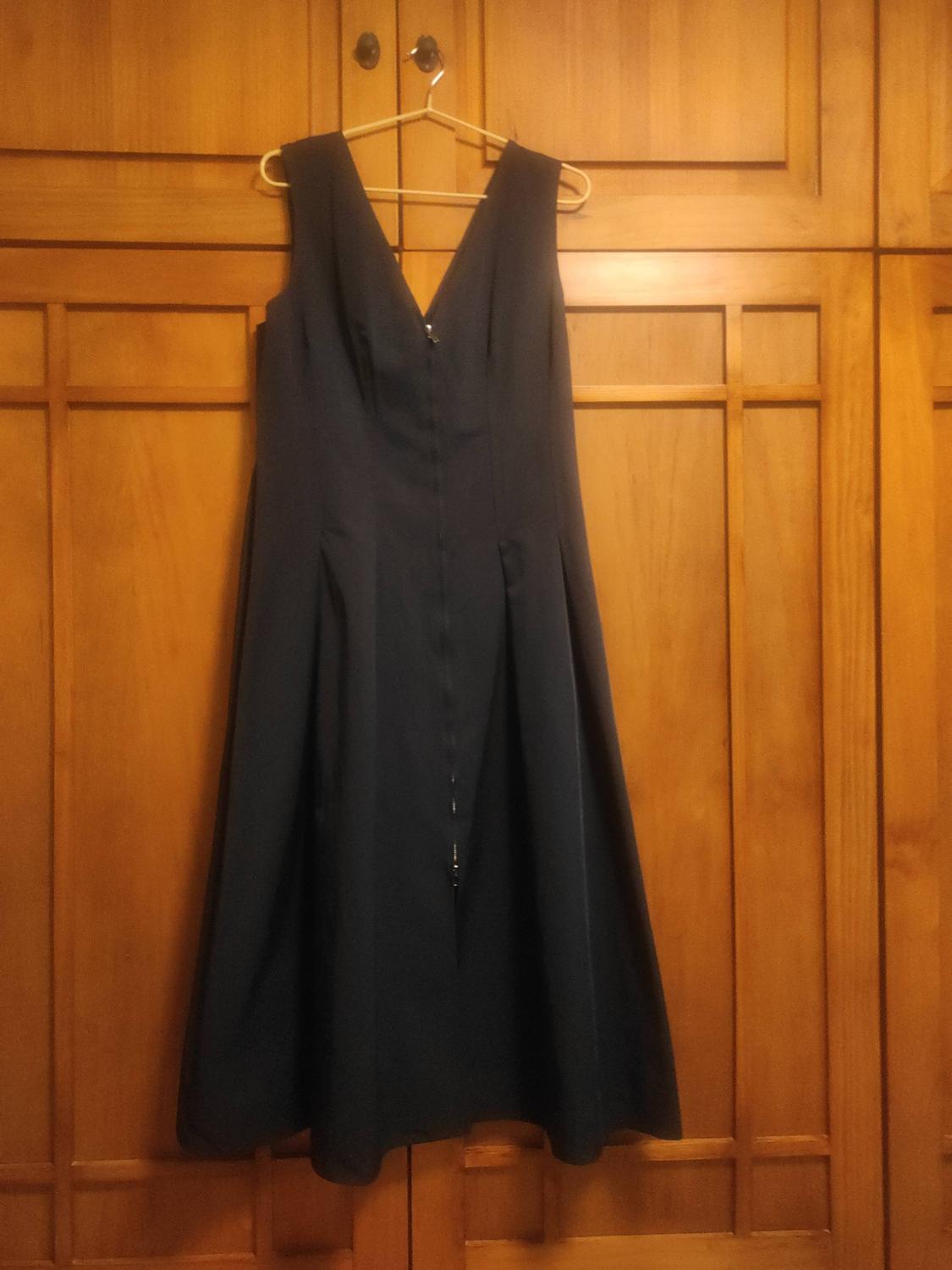 Dark sleeveless dress with a V-neck and pleated skirt, hanging on a hanger in front of a wooden wardrobe.