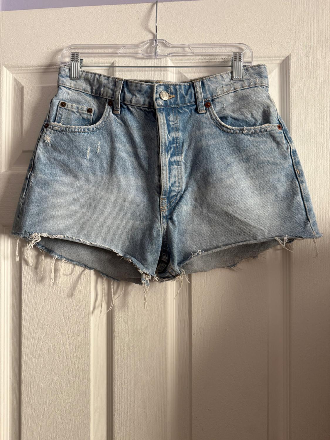 Worn light blue denim shorts, hanging on a clear hanger over a white door.