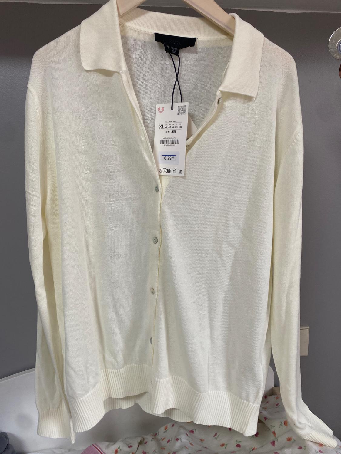 White, long-sleeved cardigan hanging on a hanger, with a visible price tag of 29.95 euros and size XL.