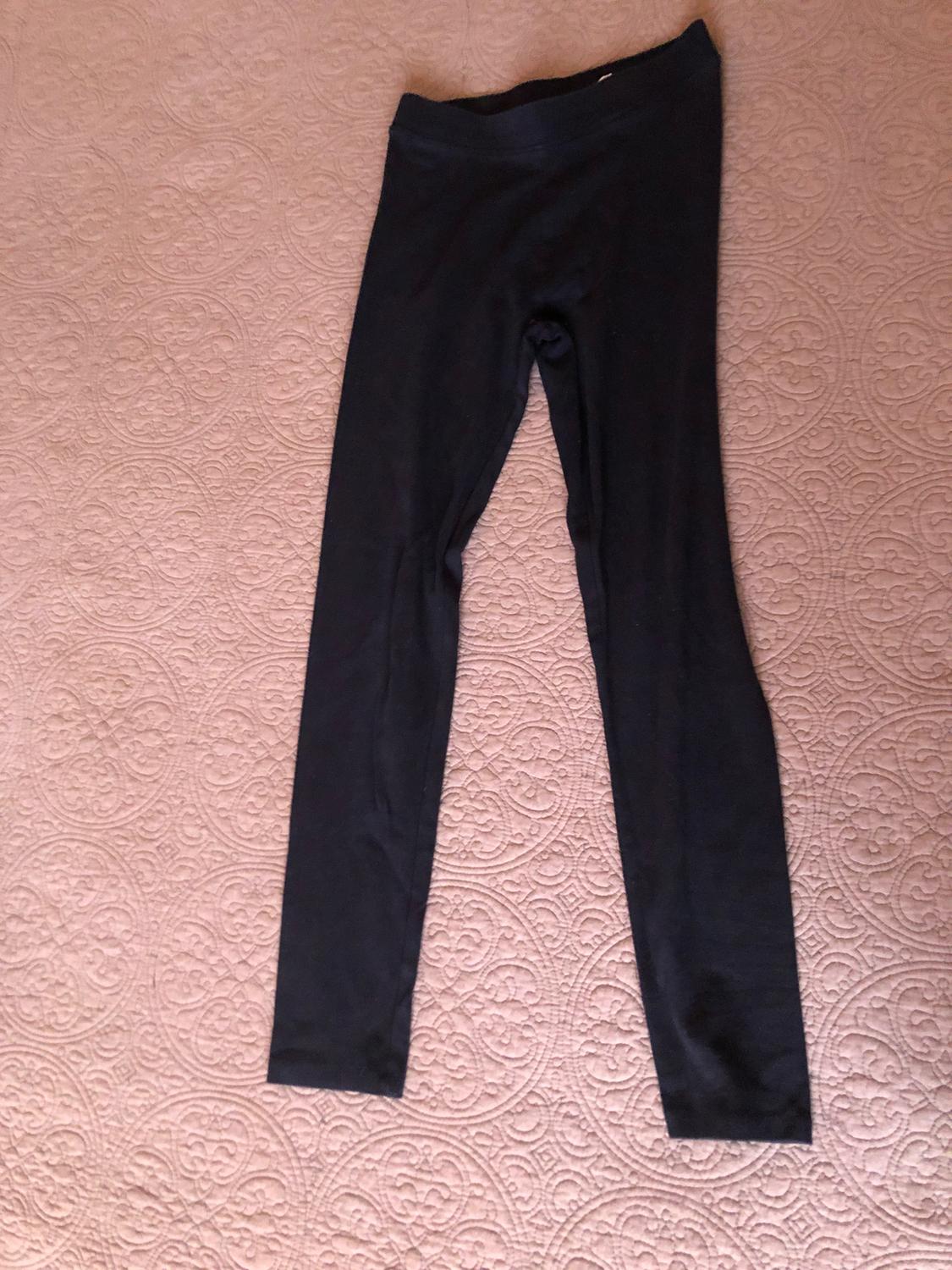 Black soft fabric trousers on a beige bedspread with a circular pattern design.