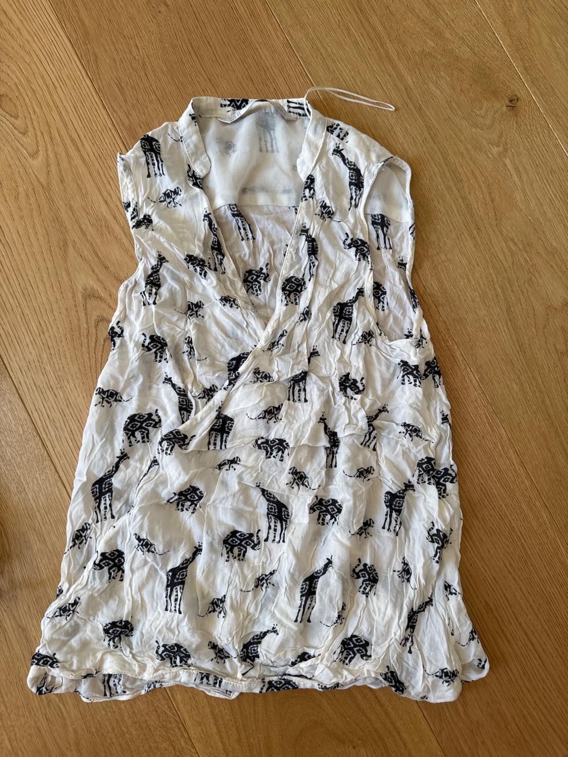 White sleeveless crinkled V-neck blouse with a black giraffe and elephant print, on a wooden floor.