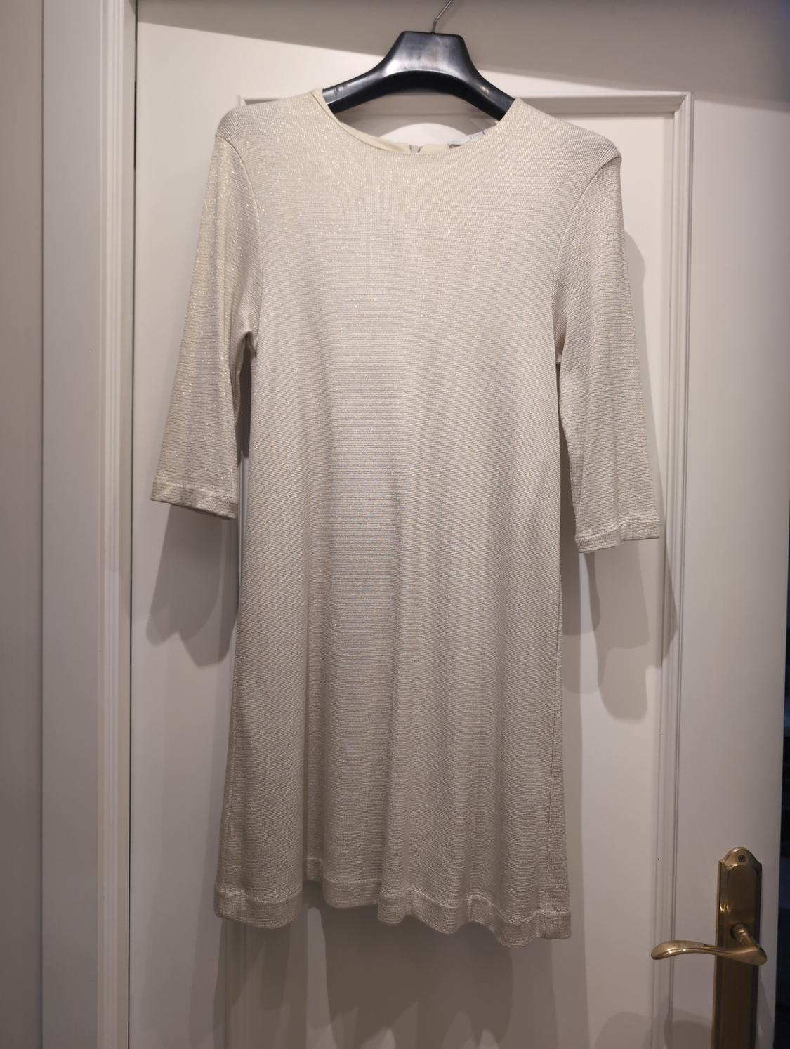Shiny beige three-quarter sleeve mini dress hanging on a black hanger over a white door with a gold handle.