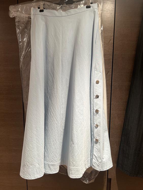 Light blue long skirt with side buttons, hanging on a hanger against a wooden background.