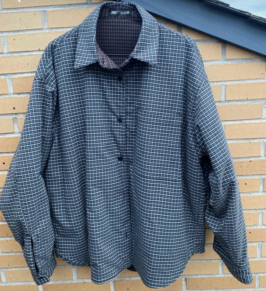 Checked shirt in dark shades hanging in front of a brick wall. Label visible on the collar.