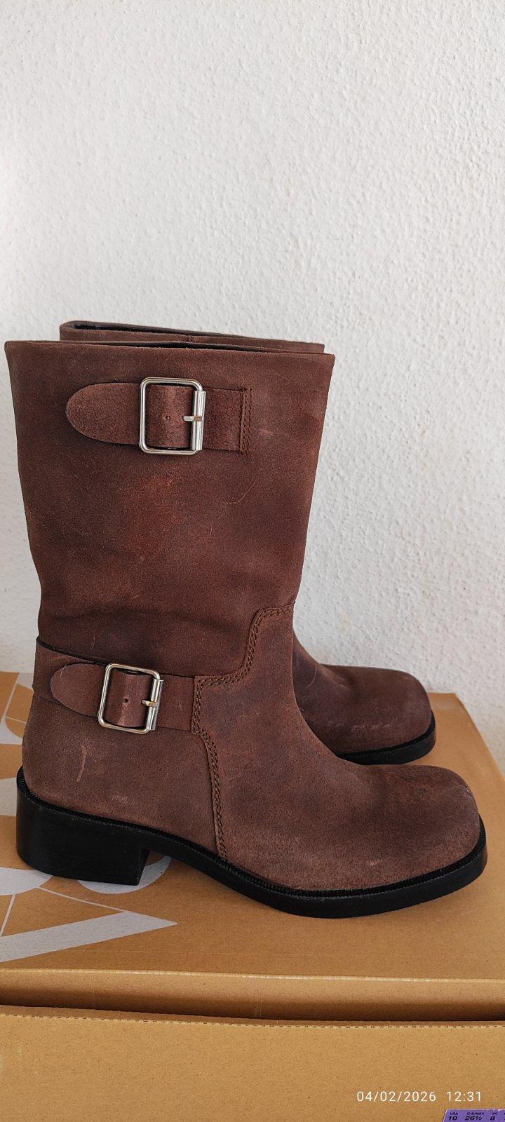 Brown suede boots with metal buckles on a cardboard box. Date and time in the bottom right corner: 04/02/2026 12:31.