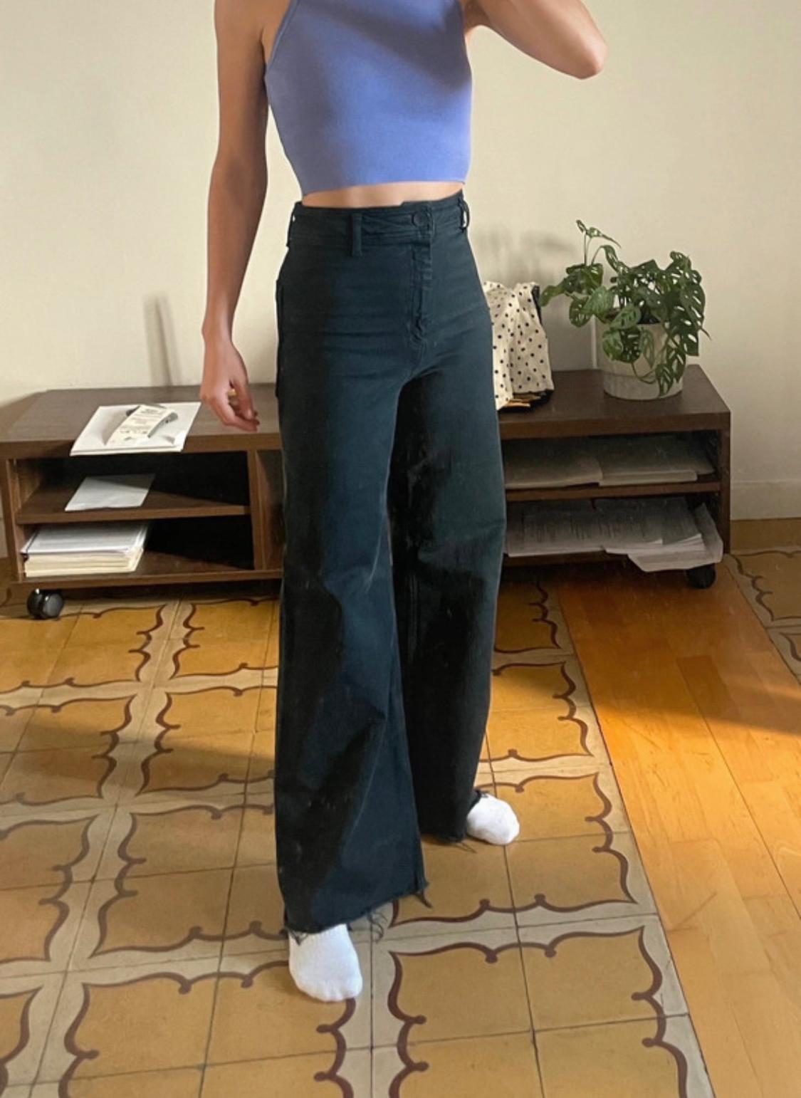 At-home model wearing a blue crop top, wide-leg black high-waisted jeans and white socks. Relaxed setting with a tiled floor.