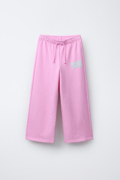 Frontansicht einer rosa Jogginghose mit elastischem Bund und Kordelzug. Text "YES OUI" auf dem linken Bein.