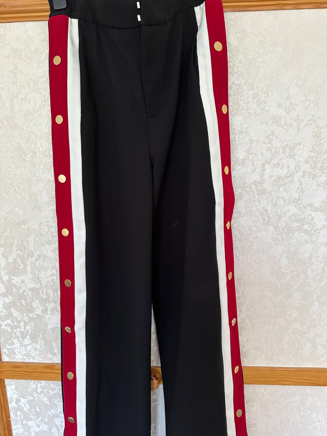 Front view of black trousers with red and white stripes and gold buttons on the sides.
