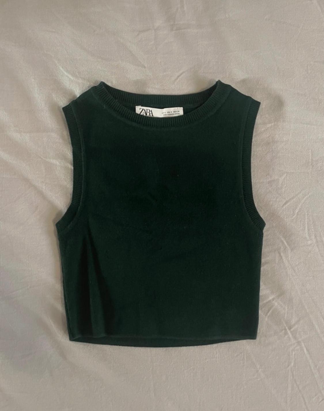 Dark green sleeveless knitted crop top with the ZARA label, on a crumpled light grey fabric.
