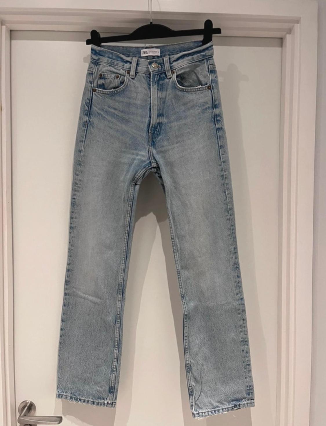 Light blue jeans hanging on a black hanger over a white door, with a visible tag on the waistband.