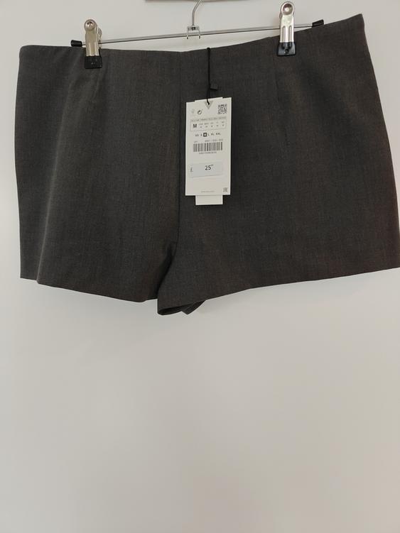 Grey shorts hanging on a hanger with a price tag of €25. White background.