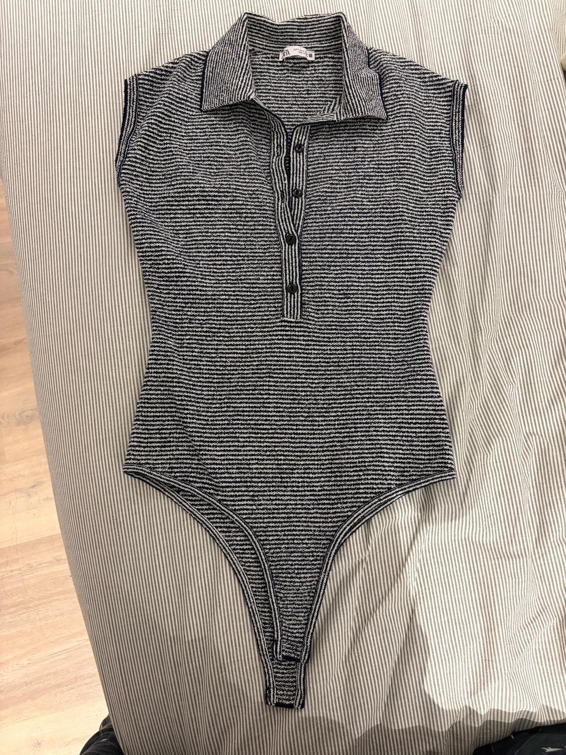 Black and white striped bodysuit with collar and buttons, on striped fabric against a light wood background.