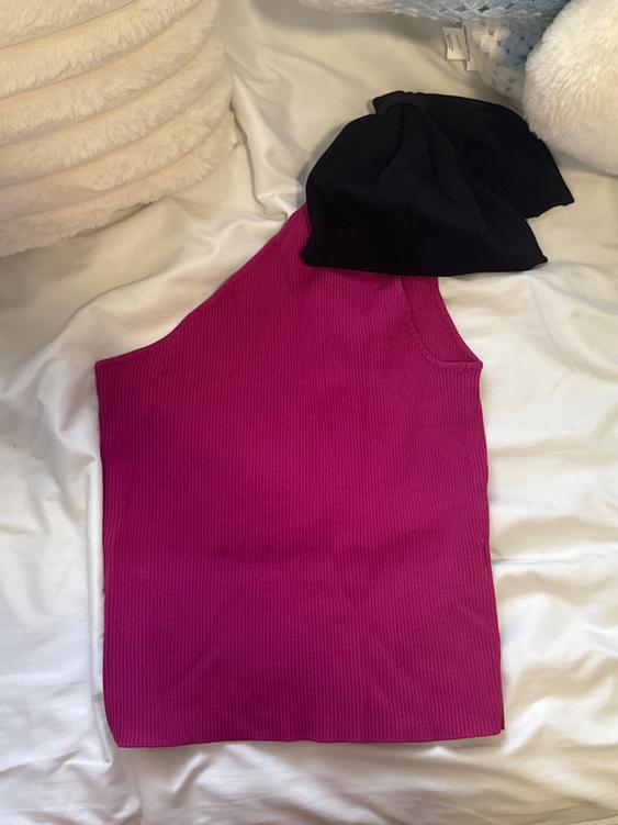 Fuchsia one-shoulder top on a white bed, with a black bow on top.