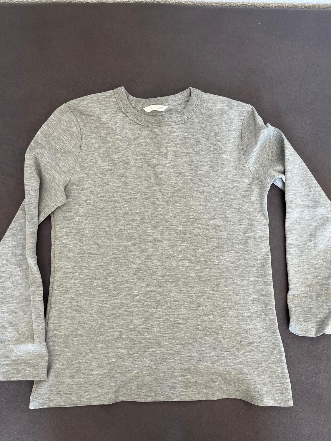Grey long-sleeved T-shirt on a dark background, with a round neck and a visible white label on the inside of the collar.