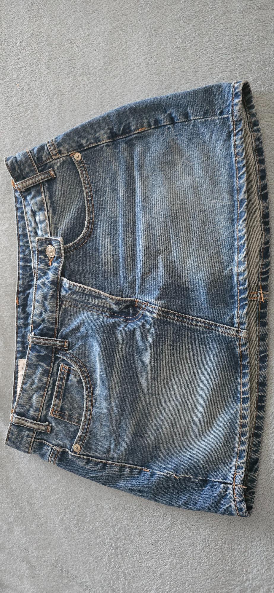 Blue denim skirt with pockets and visible stitching, on a light grey background.