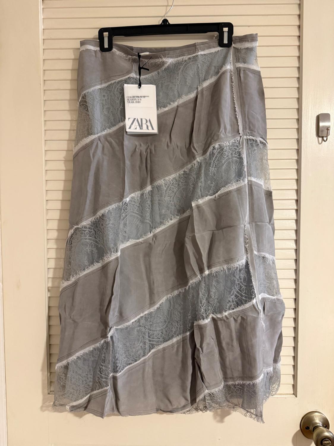 Grey skirt with diagonal lace panels, hanging on a black hanger. Visible label with the text "ZARA". White door background.