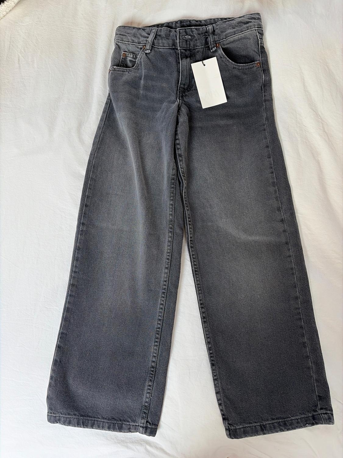 Grey wide-leg jeans with a white hang tag, on a white surface.