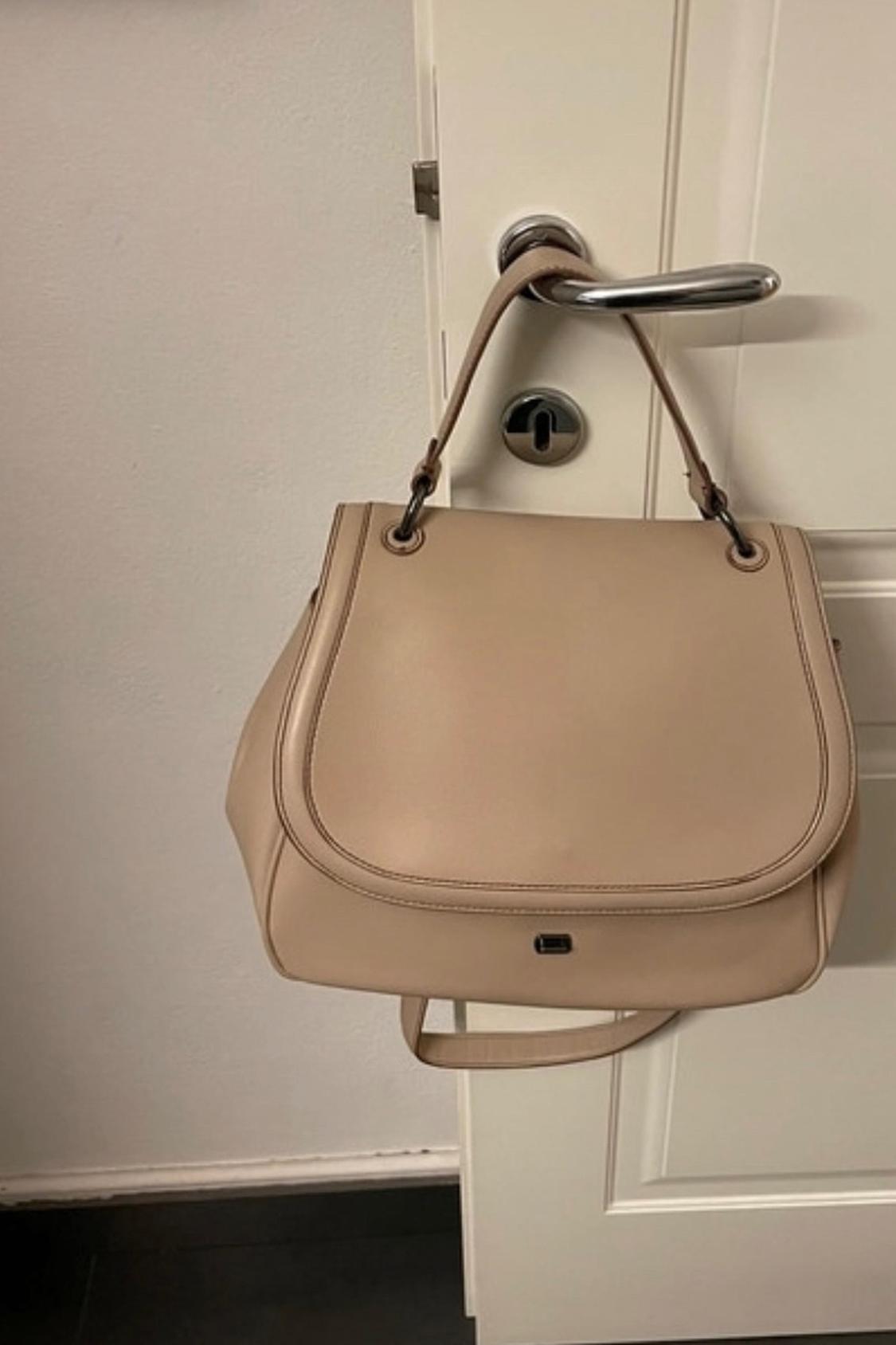 Front view of a beige handbag with a handle hanging from a door handle.