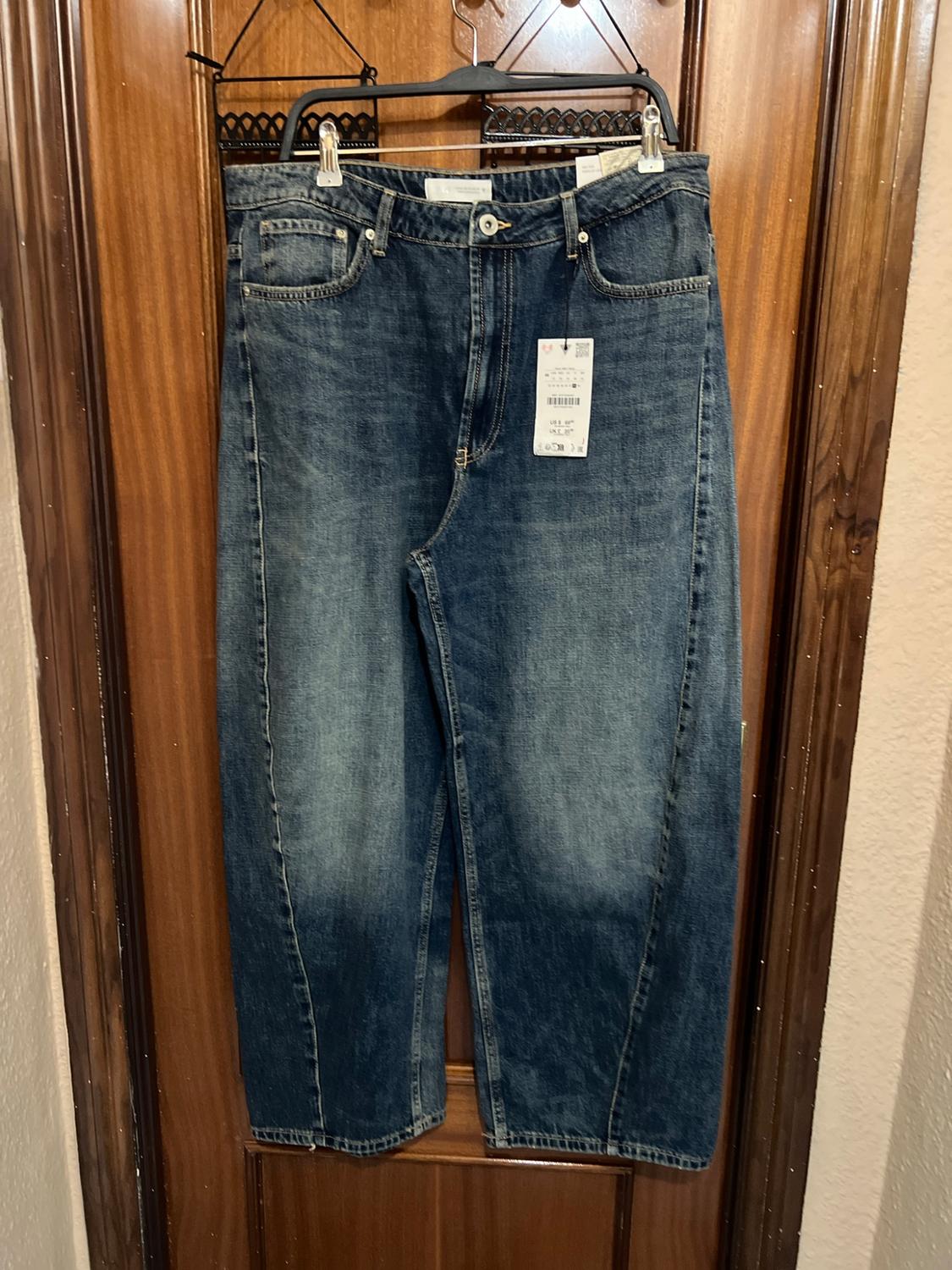 Blue wide-leg jeans with front seams and a washed effect, hanging on a hanger on a wooden door.