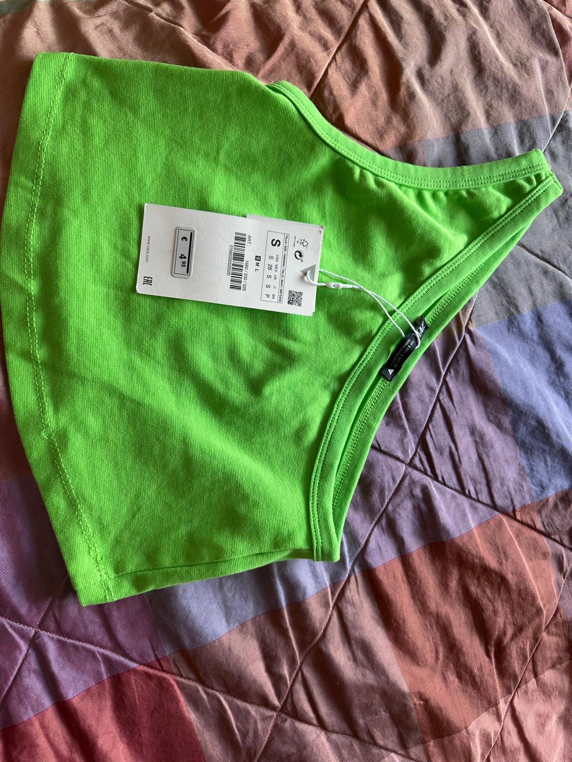 Bright green ribbed asymmetric top on a bedspread. Label with text: S, € 4.95, www.zara.com, EAC, ART: 1660/330/520.