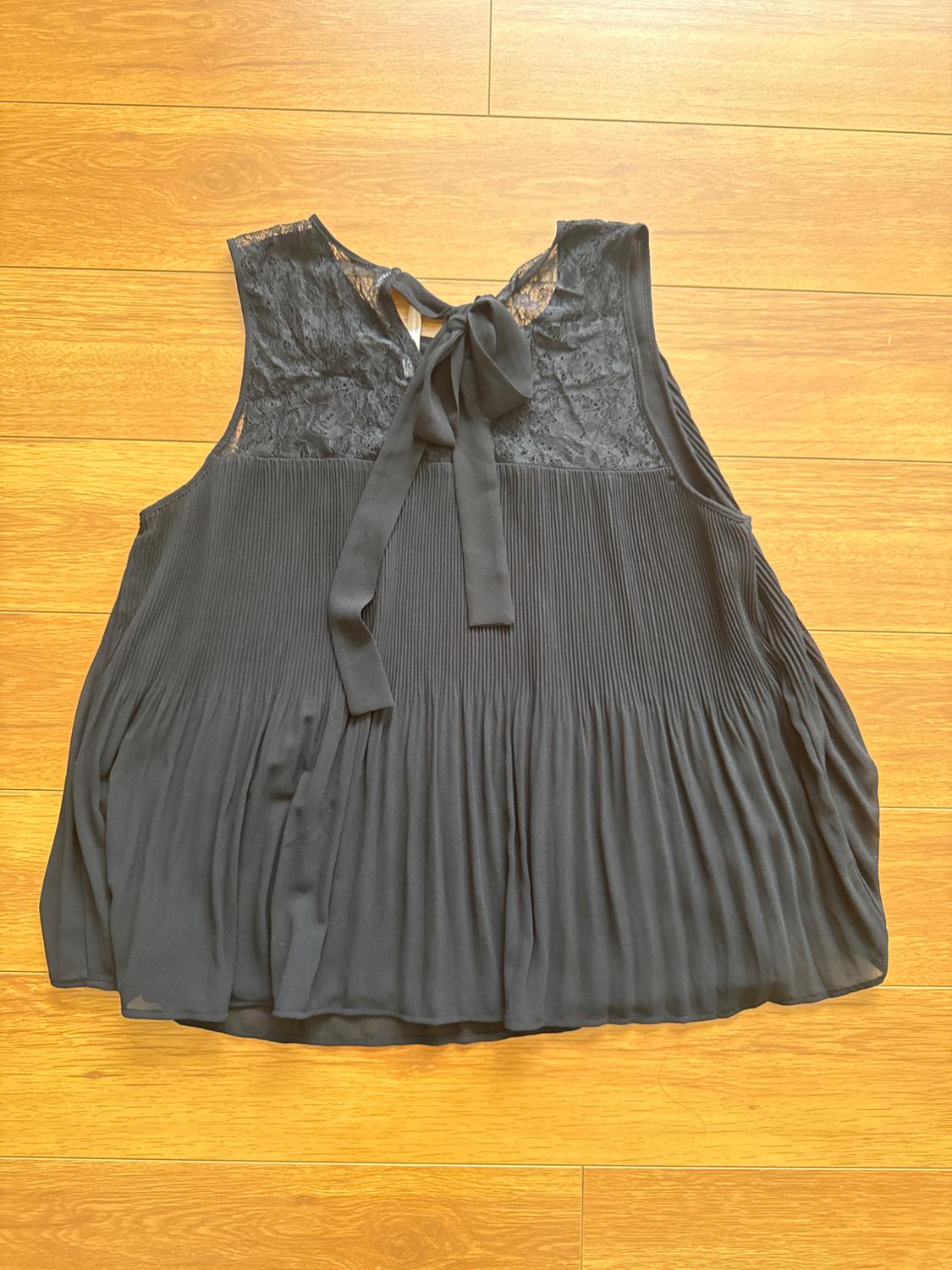 Sleeveless black blouse with lace on the top and a bow at the back, on a light wooden floor.