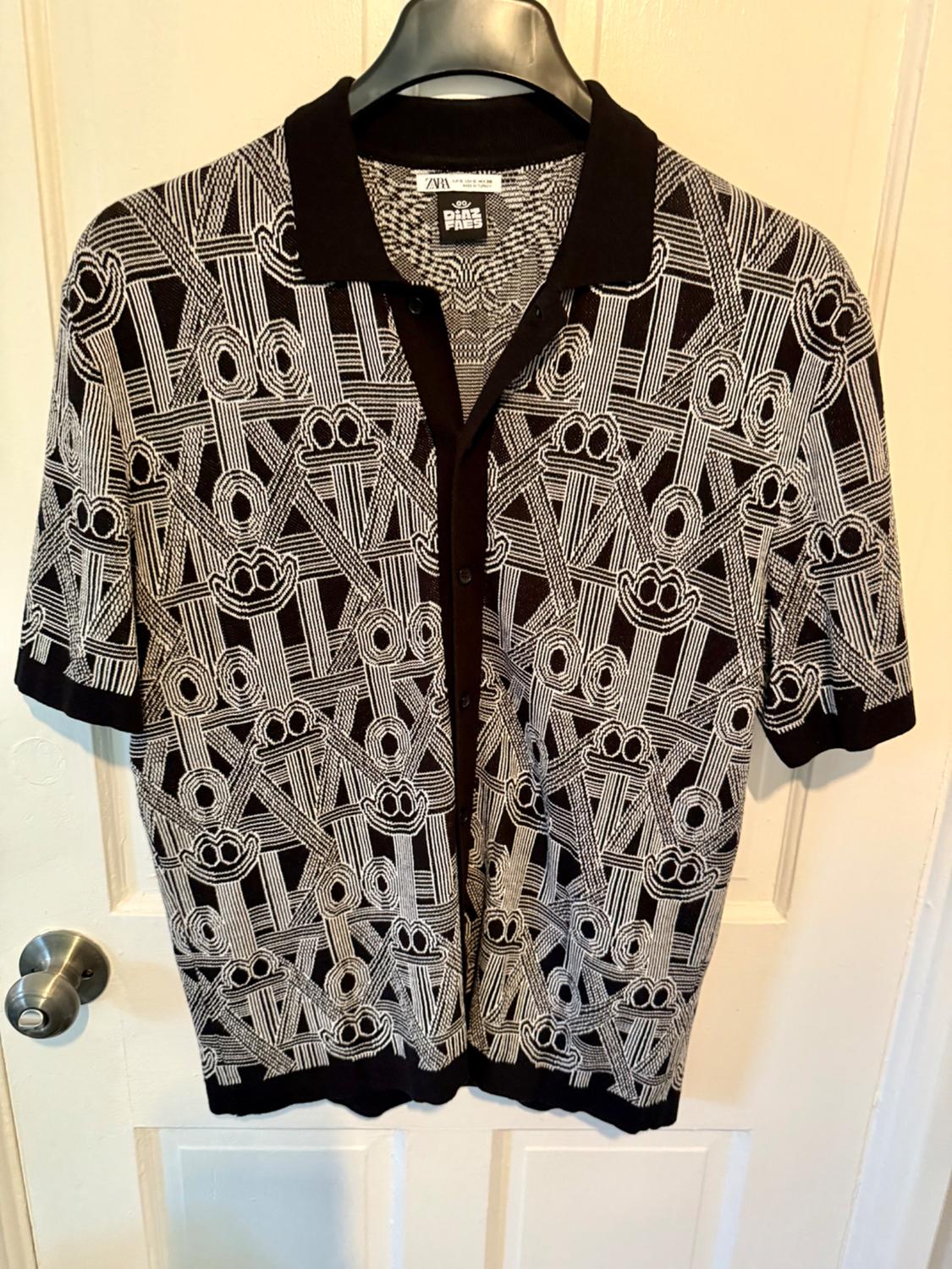 Shirt hanging on a hanger with a black and white geometric print, black background and black collar. Label visible on the collar.