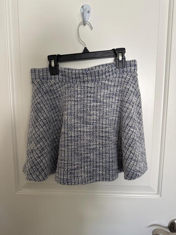 Gray and blue ribbed fabric mini skirt, hanging on a black hanger over a white door.