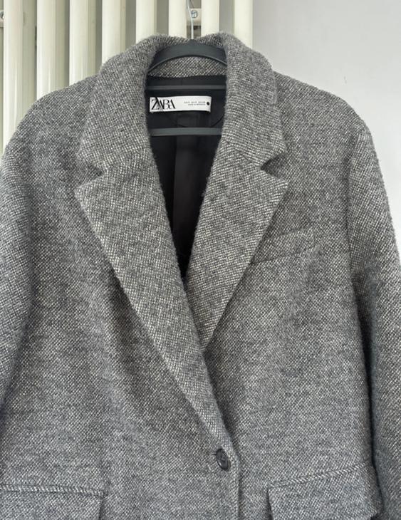 Textured grey coat hanging on a hanger, with visible label that says "ZARA". White radiator background.
