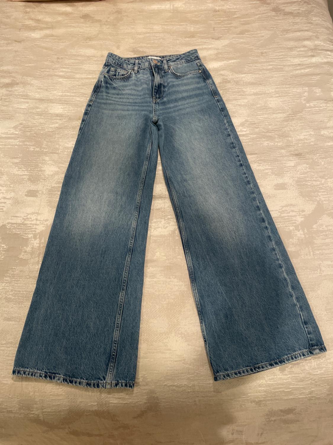 Light blue wide-leg jeans, placed on a textured beige surface.