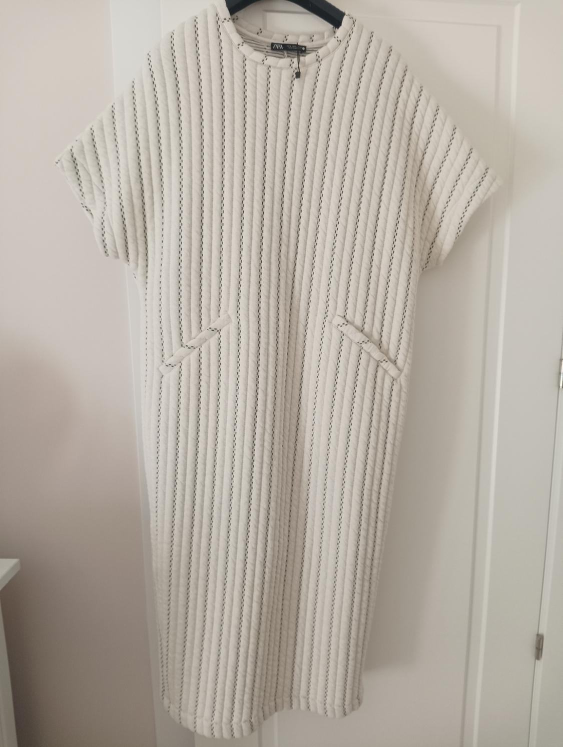 White vertical striped dress hanging on a black hanger over a white door.