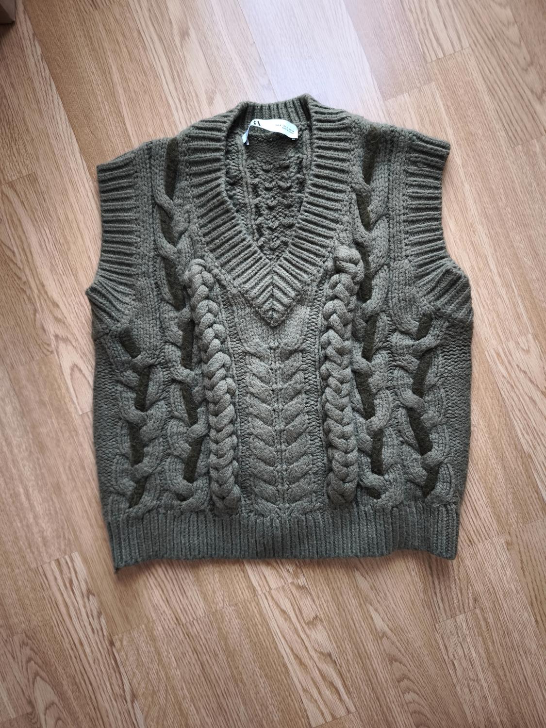 Chunky brown knitted waistcoat with cable knit design, V-neck, on a light wood floor.