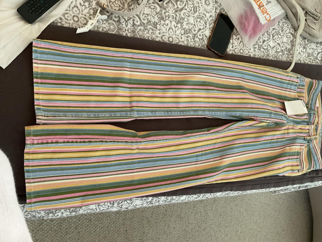 Multicolor striped pants with tag, laid out on a bed. Relaxed setting including a mobile phone and a remote control.